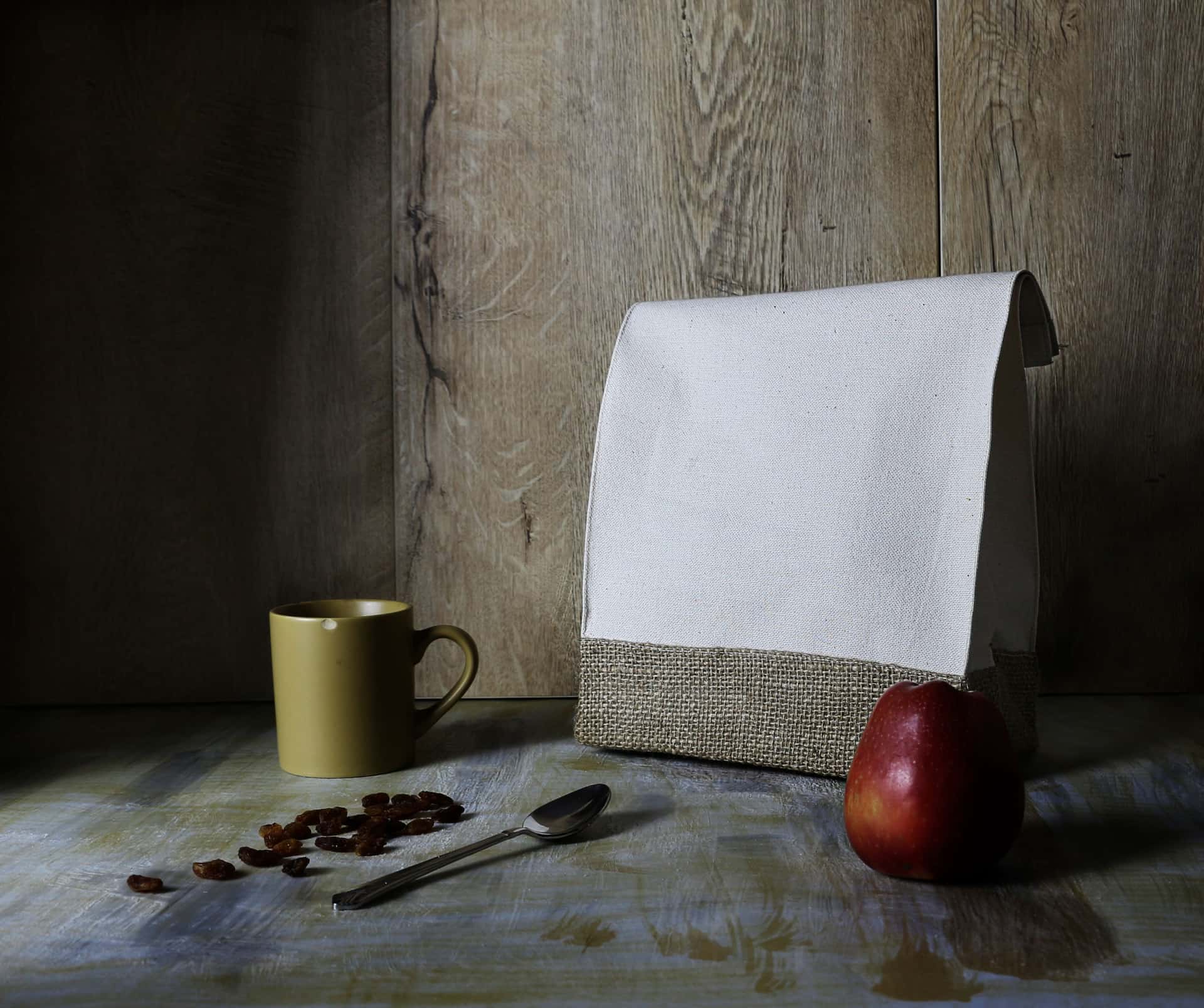 A dark canvas work backpack and an insulated lunch bag standing against a warm wall