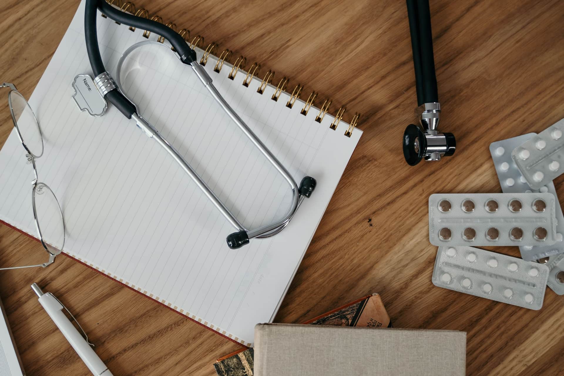 Trauma shears, a penlight, a badge reel and pens laid out in a flat-lay on warm wood